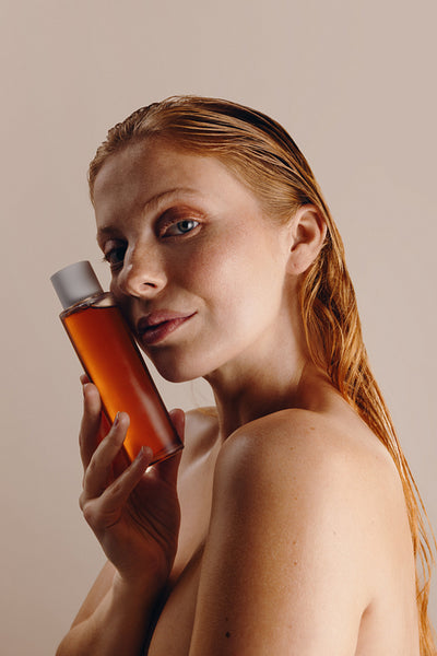 Woman holding amber glass skincare bottle in studio portrait