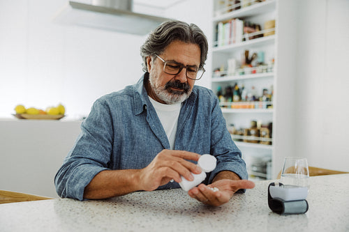 Taking medication, senior man pours pills with water