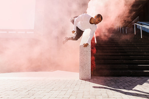 Man practicing parkour in urban space with smoke grenade