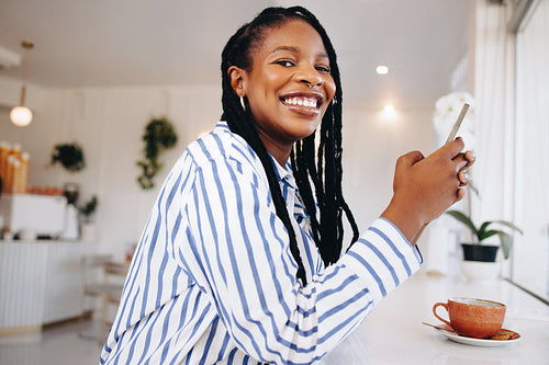 Happy young woman using a smartphone during her coffee break in a cafe