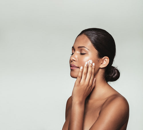 Beautiful young woman applying moisturizer to her face