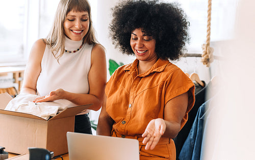 Two happy young women preparing a delivery parcel in a thrift store