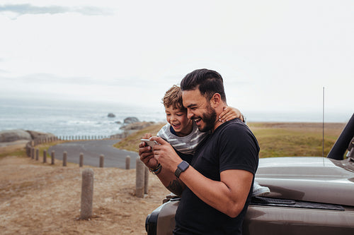 Happy father and son in front of the car using smart phone