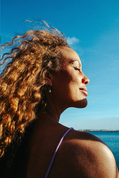 Sunlit woman basks by the water with eyes closed in summer