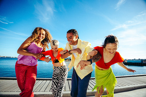 Diverse friends dance arm in arm by the waterfront on a sunny day