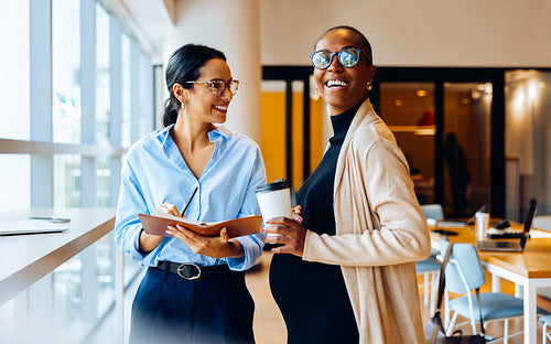 Two professional women smiling and engaging in a friendly conversation at the office