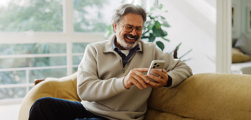 Senior man uses a smartphone while relaxing at home