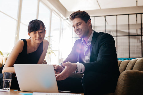 two businesspeople using laptop in lobby of modern office