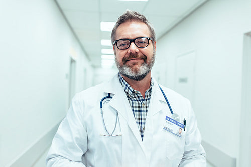 Happy mature male doctor standing in hospital corridor