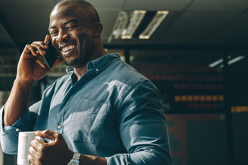 Smiling businessman with coffee talking on cellphone