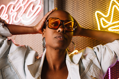 Stylish woman with sunglasses posing confidently in neon light studio