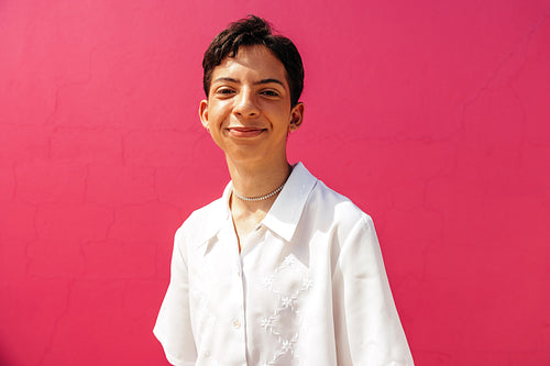 Smiling teenage boy standing against a pink background