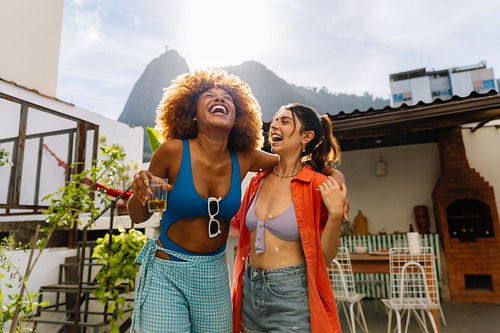 Two women laughing together outdoors in a sunny Rio de Janeiro backyard