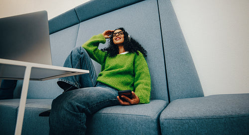 Woman relaxing in casual workspace with smartphone and laptop