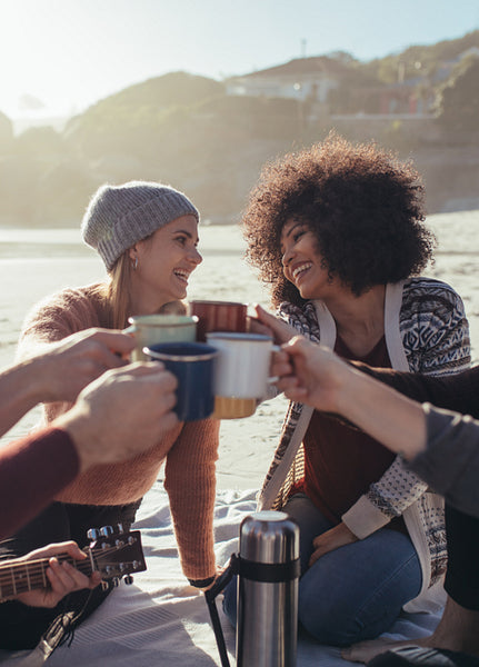 Friends toasting coffee cups at the beach