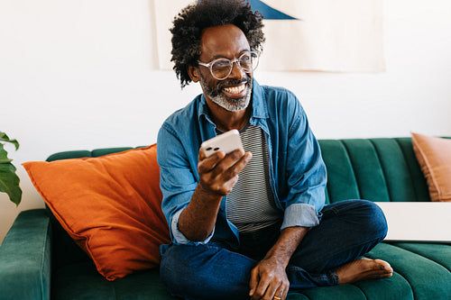 Happy mature man relaxing on the sofa, smiling and using a mobile phone