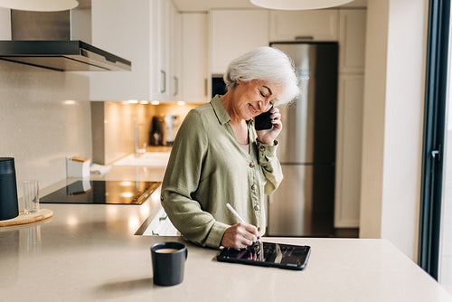 Senior businesswoman making notes during a phone call at home