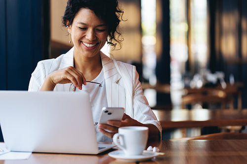 Professional woman texting on smartphone while working on laptop at cafe