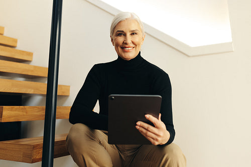 Mature business woman smiling at camera while working with tablet in office