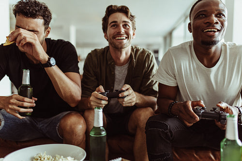 Male friends playing video game sitting at home with snacks