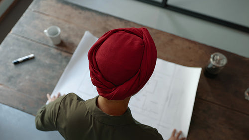 Female architect in a headscarf reviewing a blueprint document in an office