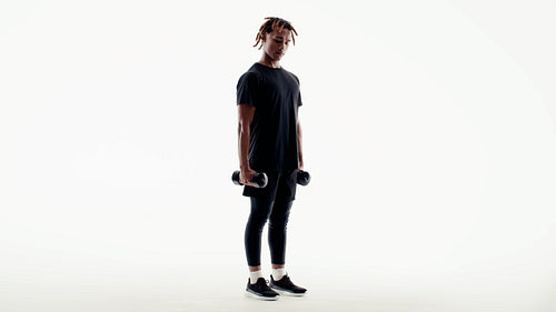 A young man trains his muscles by lifting dumbbells in a bright studio