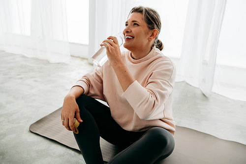 The woman enjoys hydration with water on her yoga mat after a home workout