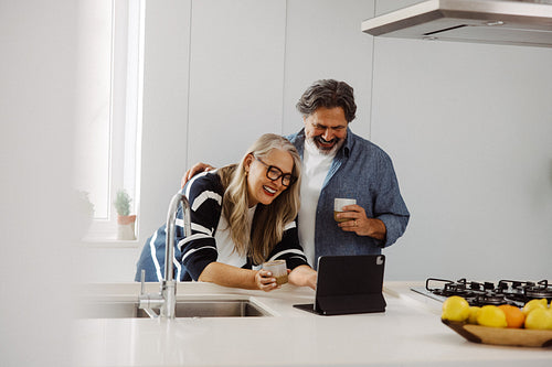 Senior couple enjoy coffee while using a tablet at home