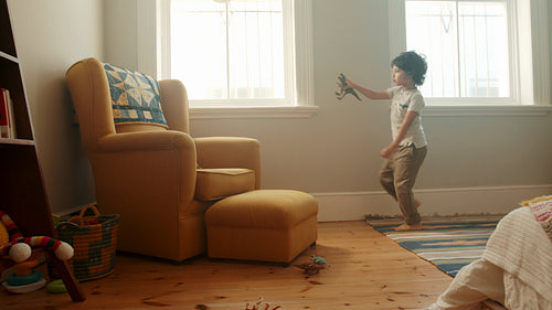 Adventurous little boy playing with a toy dinosaur in his room at home