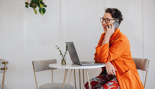 Cheerful businesswoman having a phone call with a client while working in a cafe