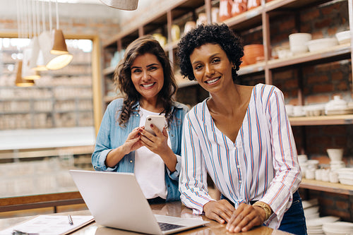 Happy female ceramists smiling at the camera while working in their shop