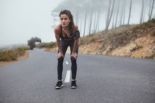 Young woman runner on the road taking a break