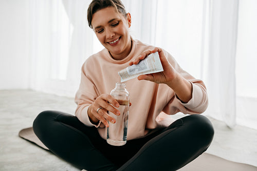 Supplement mixing becomes the woman’s hydration routine on a yoga mat after workout