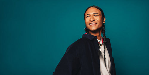 Confident ethnic man smiling against blue background with stylish braided hair and jewelry