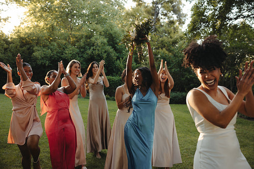 Bridesmaids celebrating a bouquet toss at an outdoor wedding gathering