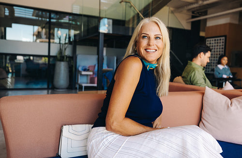 Smiling blonde woman sitting on a couch in a modern workspace