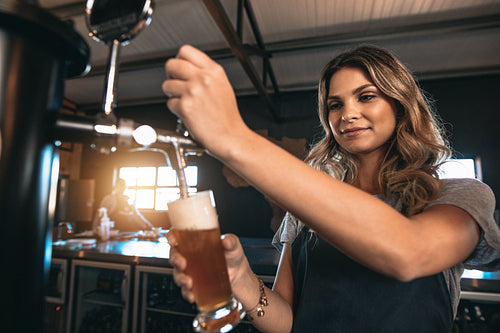 Beautiful female bartender tapping beer in bar