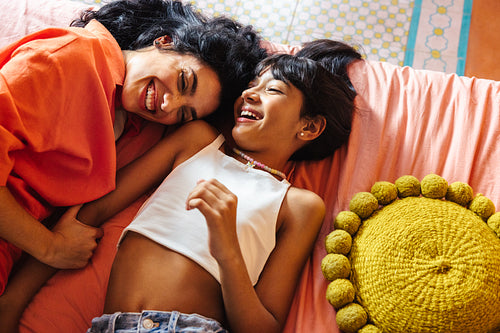 Mother and daughter laughing together on a cozy and colorful bedroom bed on Mother's day