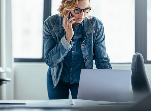 Businesswoman working on laptop and talking on mobile phone
