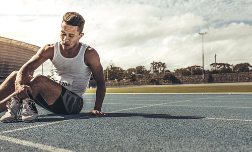 Runner sitting on running track holding his shoes