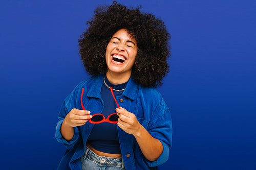 Carefree young woman laughing happily while holding sunglasses
