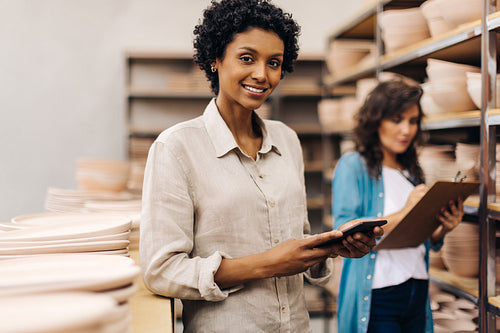 Happy female ceramist using a digital tablet in her shop