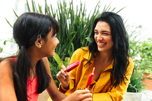 Latina mother and daughter enjoying popsicles and laughing together outdoors