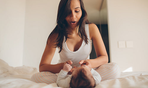 Woman sitting on bed and playing with her baby
