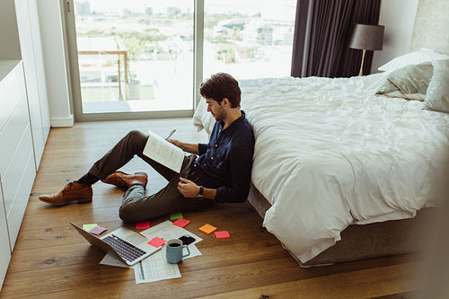 Male worker taking notes and drinking coffee working from home