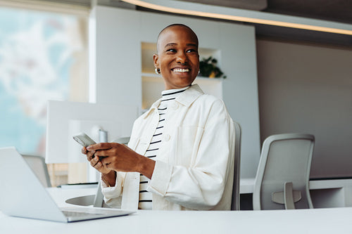 Cheerful young businesswoman working with a smartphone and a laptop at her office desk