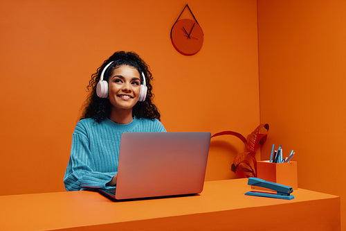 Smiling woman student studying with laptop wearing headphones in color blocking setting