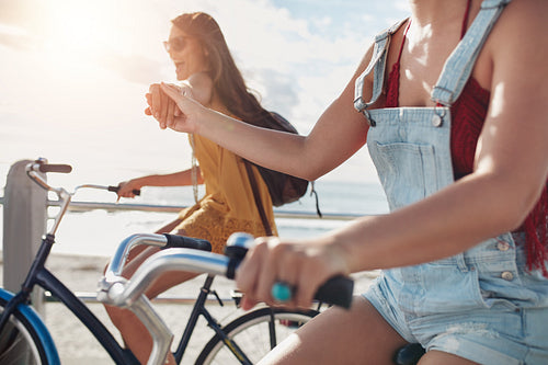 Two female friends holding hands and riding cycles