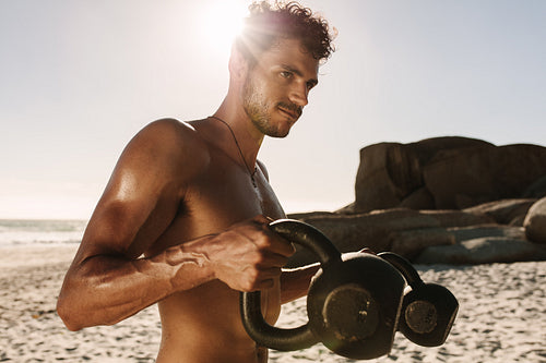 Man doing fitness training at the beach using kettlebells