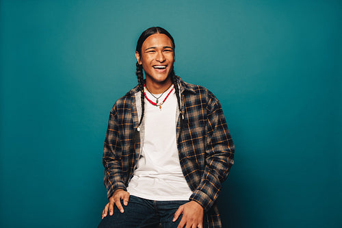 Happy and confident ethnic man with stylish braided hair and jewelry, smiling and laughing in studio